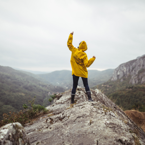 girl standing on mountain raising hand in triumph